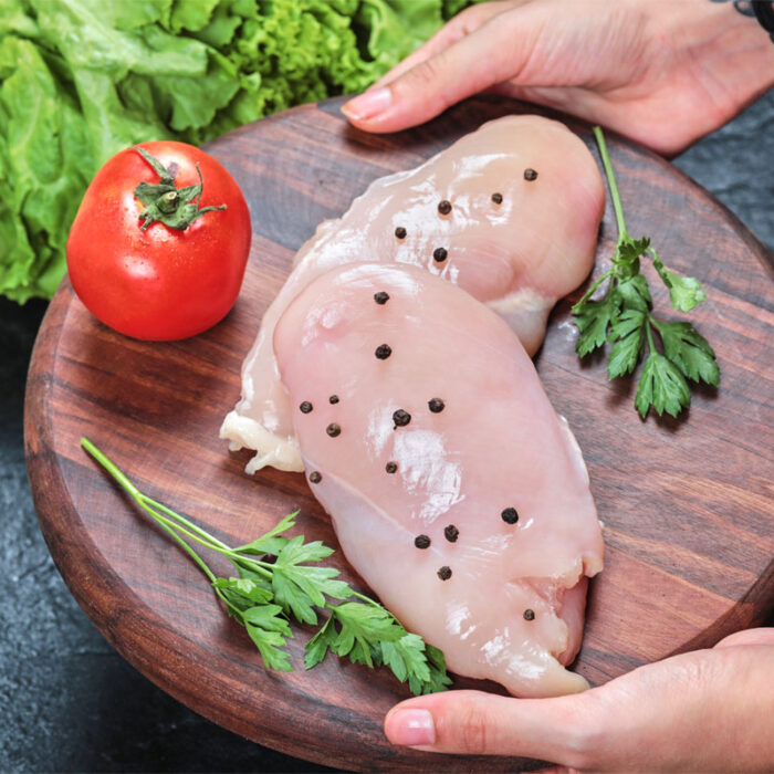 Hand holding wooden plate of raw chicken fillet with greens on dark table Escalope de poulet (le Kg) – Image 1